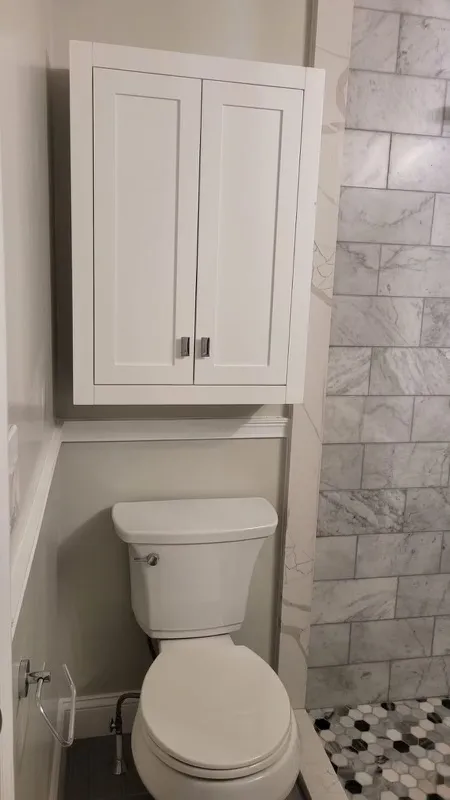 Compact bathroom with white cabinet storage and marble tile