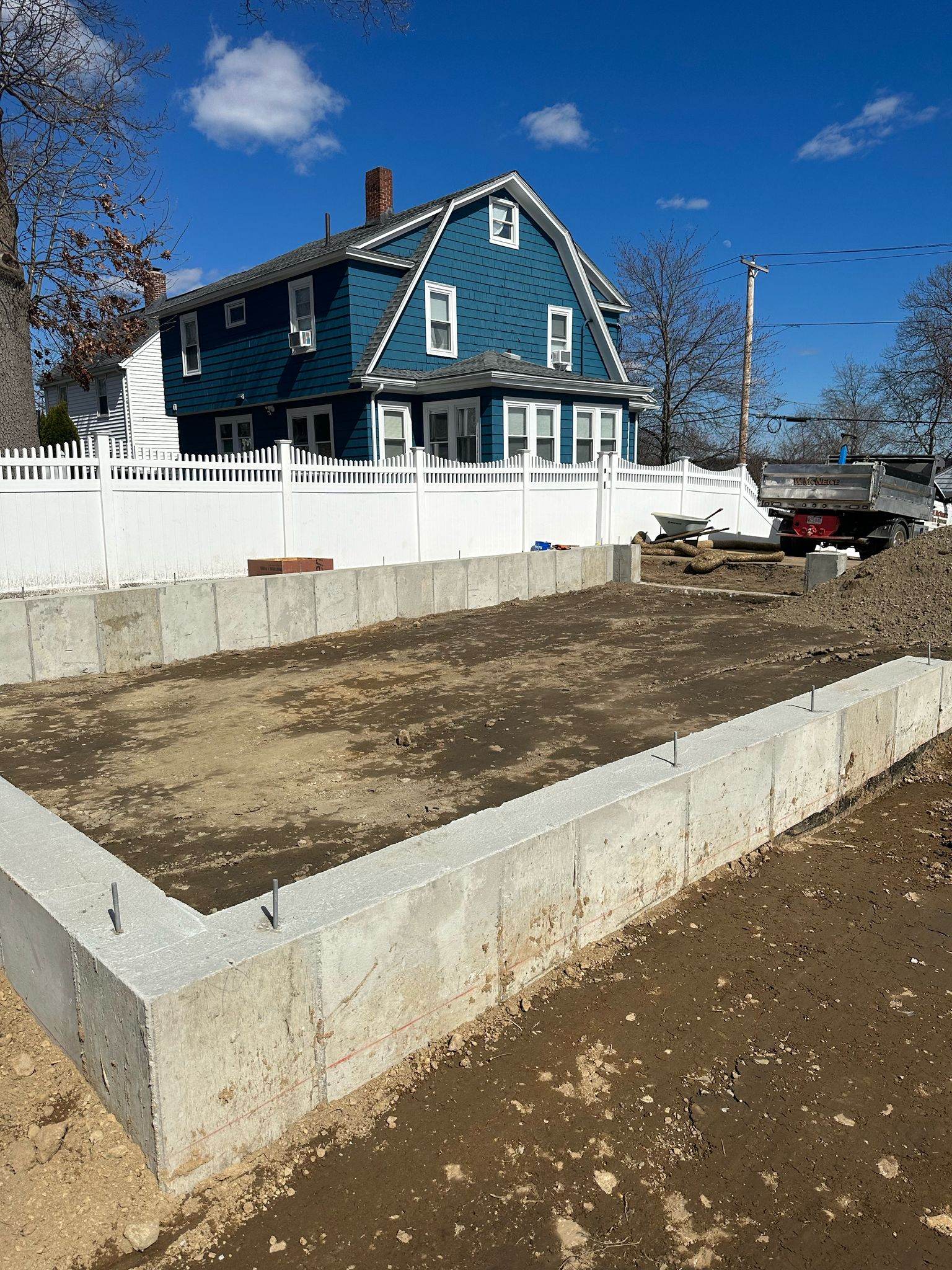Blue house with fresh concrete foundation work and white fence