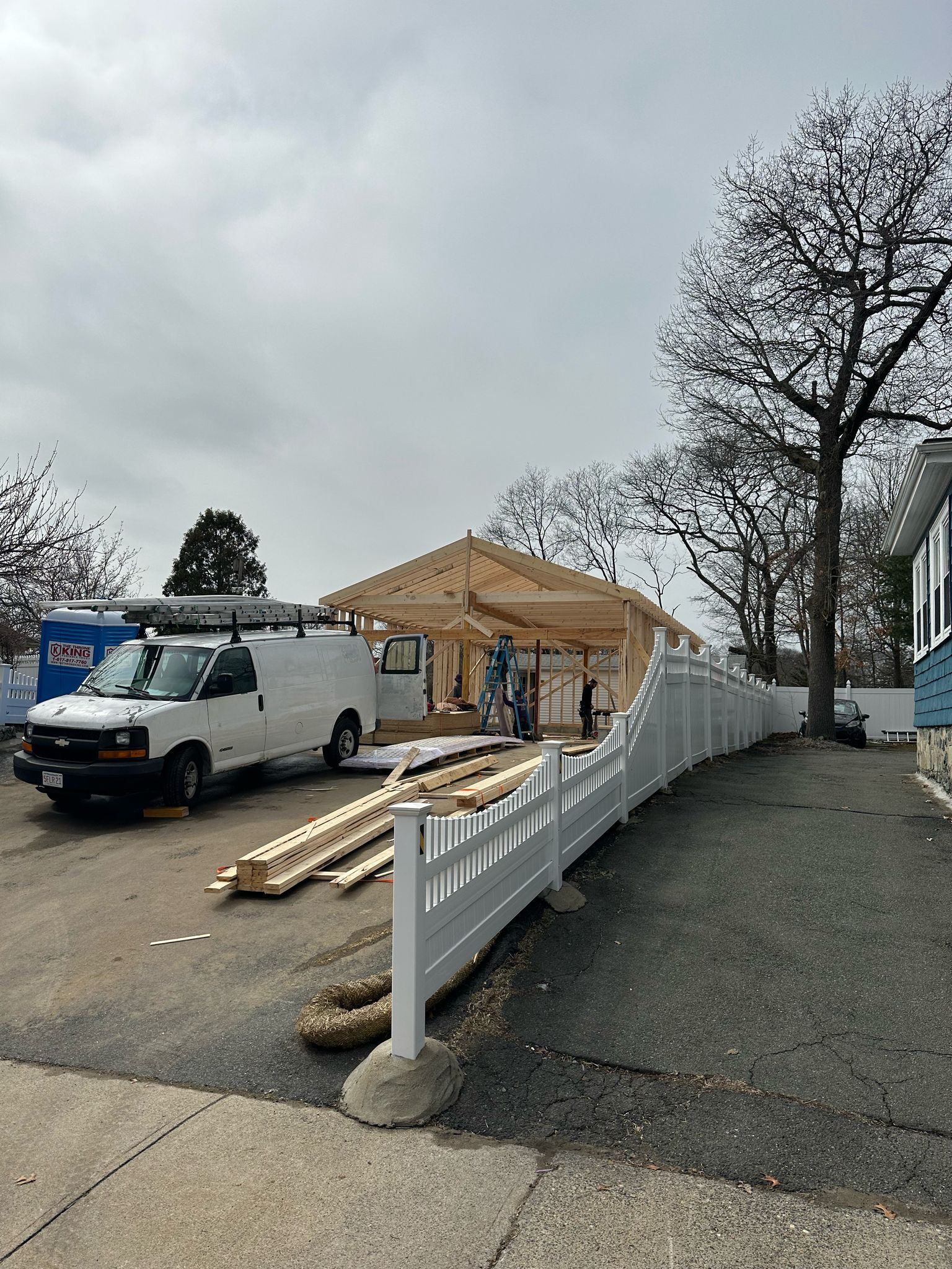 Garage addition under construction with white vinyl fence