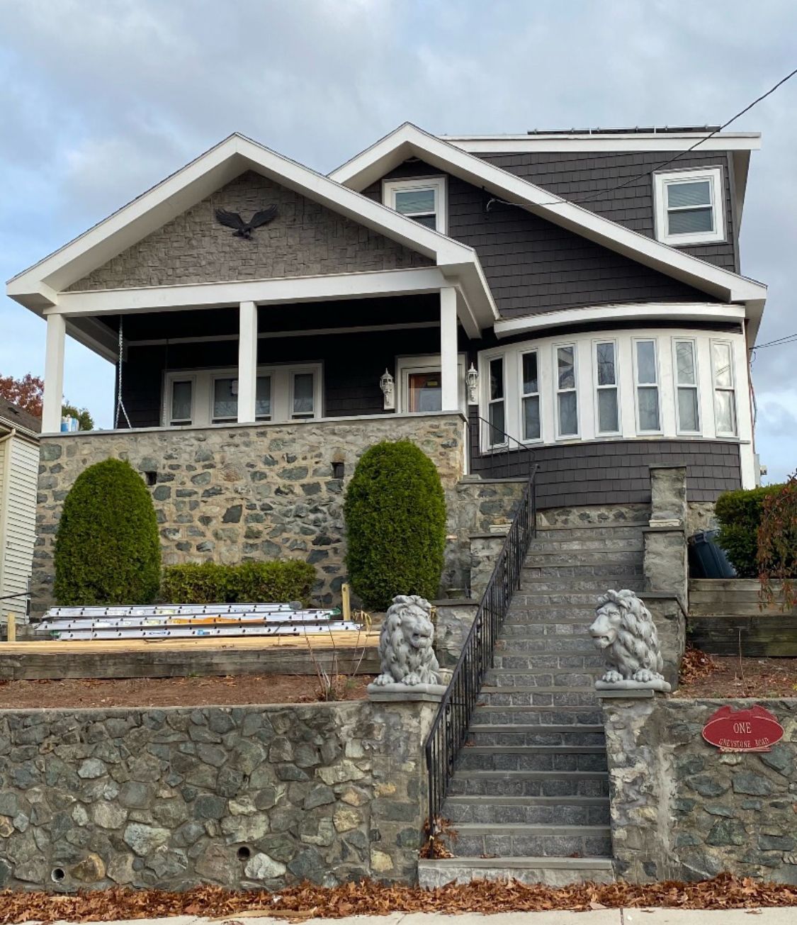 Dark gray craftsman house with stone foundation and decorative lion statues