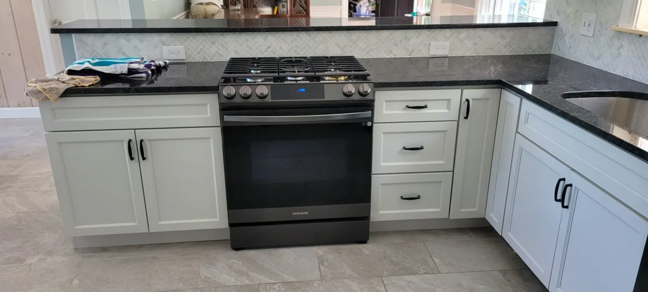 Contemporary white kitchen with dark countertops and herringbone backsplash