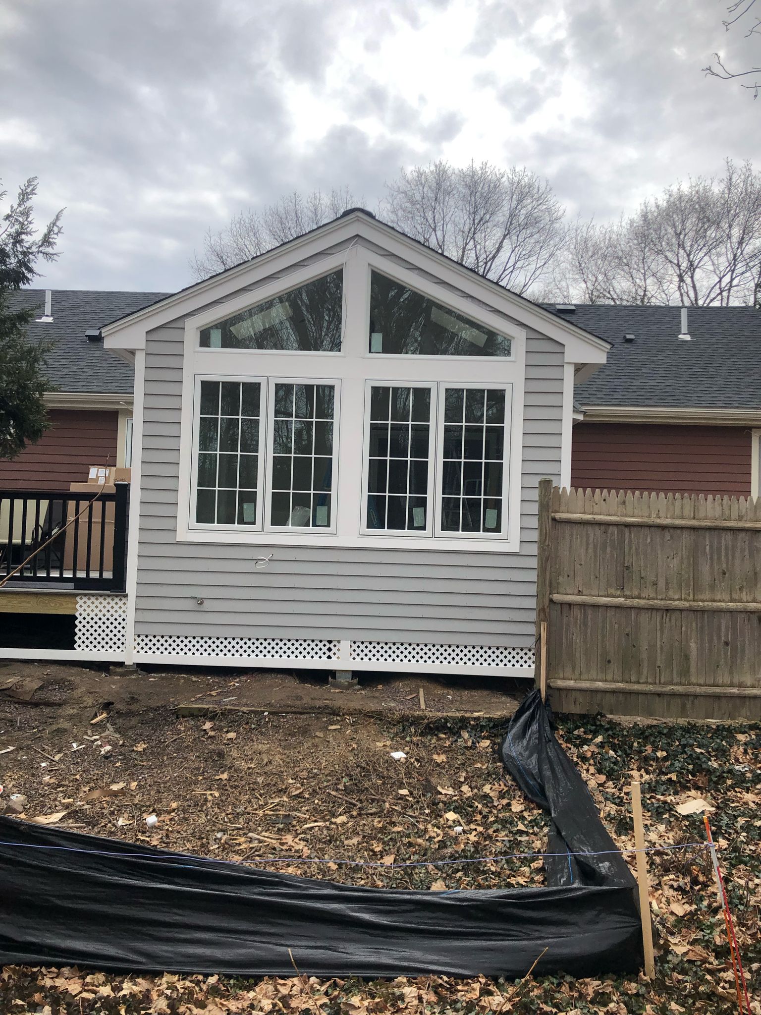 Sunroom addition with gray siding and large picture windows under construction