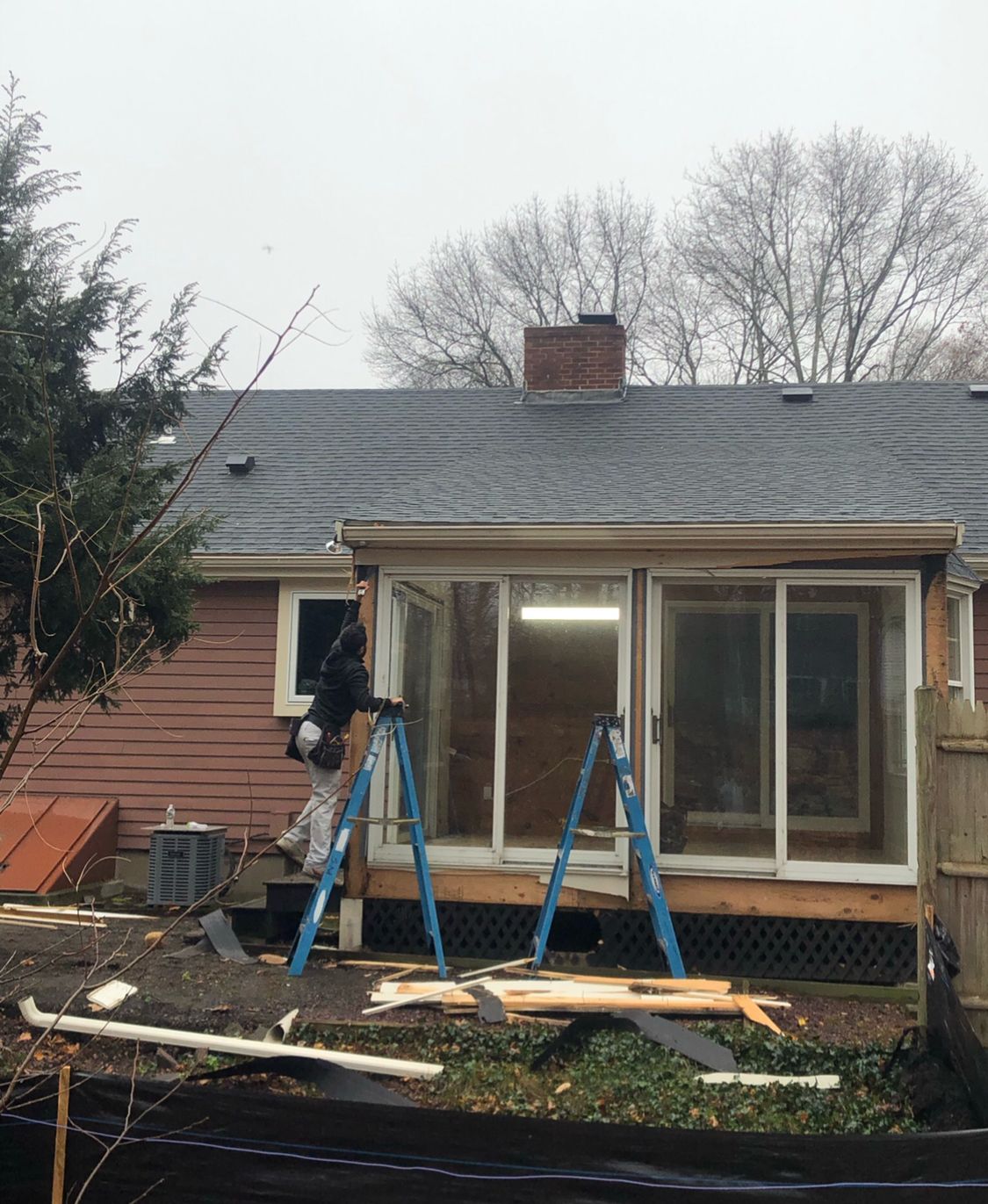 Worker installing sliding glass doors on home addition with brown siding