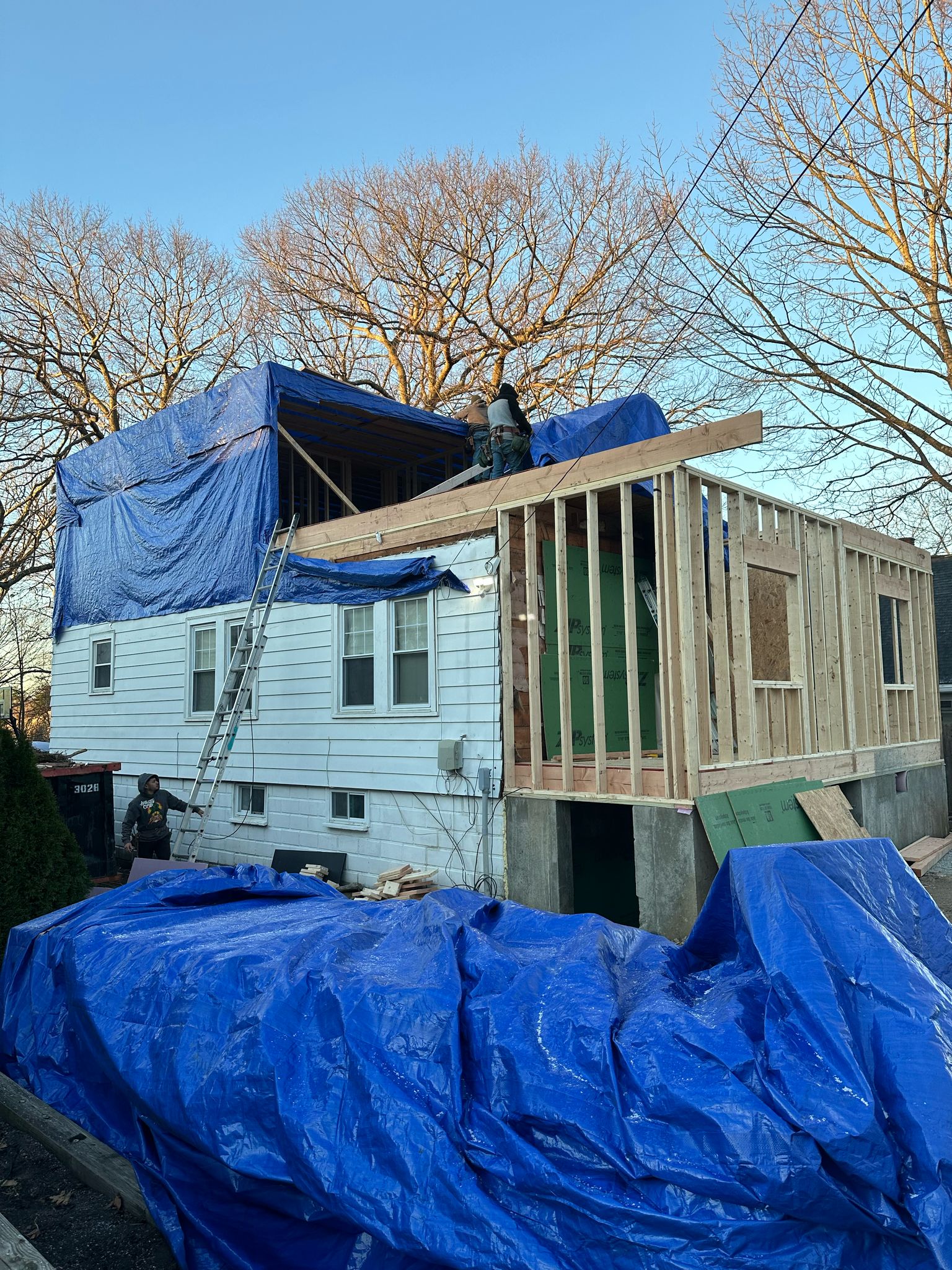 House addition framing with blue tarp protecting roof area during construction