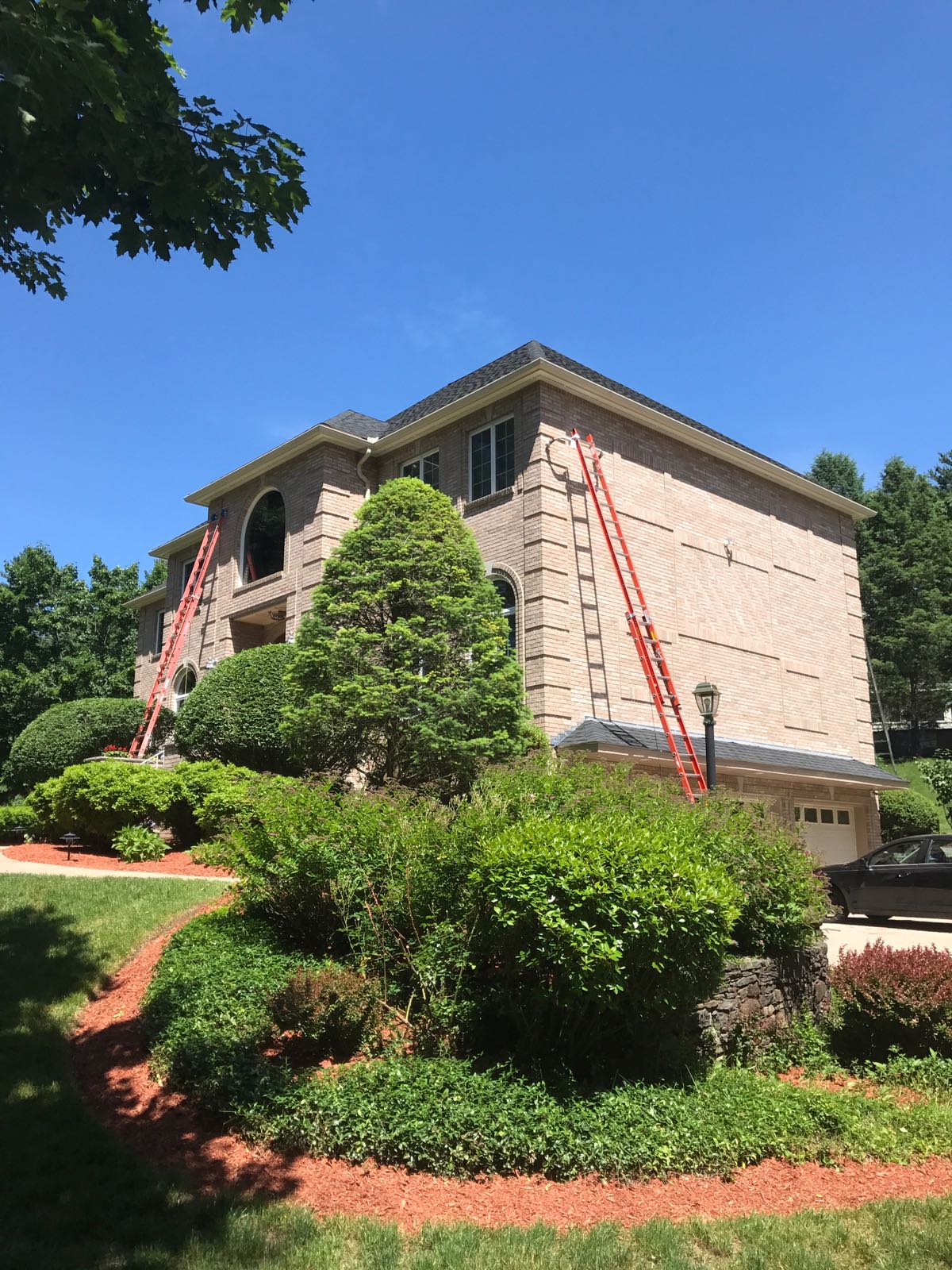 Large brick house with roofing work in progress, red ladders against the building